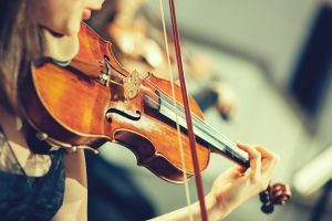 Symphony orchestra on stage, hands playing violin. Shallow depth of field, vintage style.