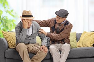 Two older men sitting on a couch, one comforting the other who is upset