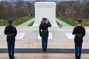 Three soldiers standing in front of The Tomb of the Unknown Soldier, saluting and honoring the soldiers represented