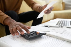 Man sitting at coffee table with calculator, adding up the cost