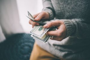 Young man wearing a gray sweater who is counting dollar bills