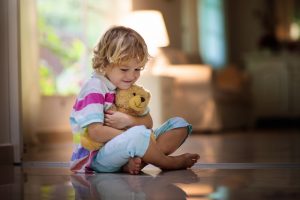 young boy sitting at home hugging a light brown teddy bear close