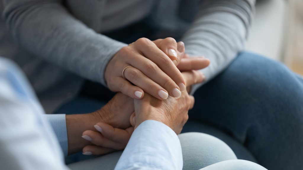 Adult daughter comforting old mom strokes holds her hand close up view.