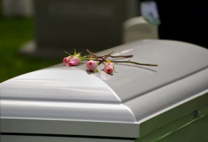 White full-couch casket with three pink flowers laying on closed lid