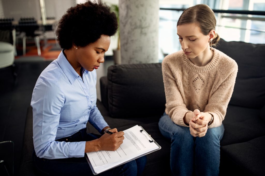 Black female funeral director taking notes during an arrangement conference with female client.