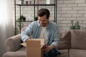 man in blue shirt opening a box while sitting on his couch