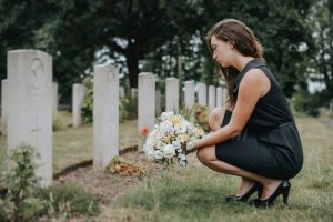 Young woman wearing black dress visits grave and leaves beautiful flowers