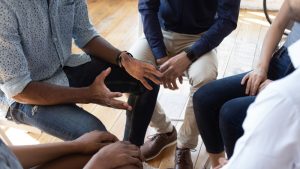 Grief support group circle of five people, image looking down at the group with focus on their hands and arms