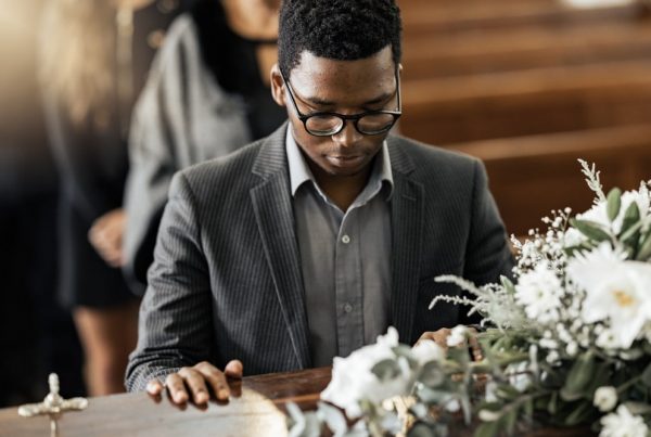 Young man standing in front of casket with his hand resting on it as he says goodbye