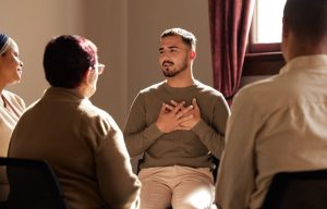 Grief support group, focus on young man who is sharing and has his hands placed over his heart
