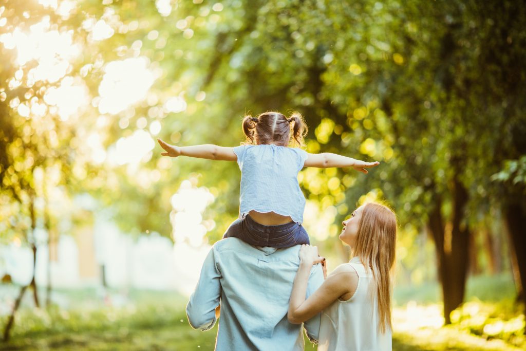 Happy family of three persons walking the grass in the park.