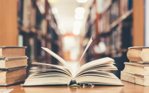 open book in a library next to stacks of books