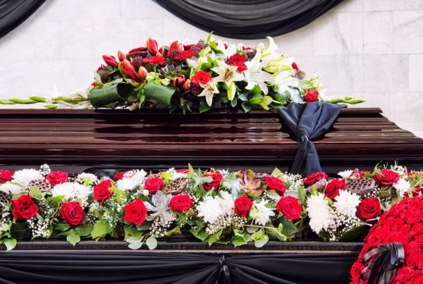 Casket surrounded by floral arrangements, including floral scarf of red and white flowers