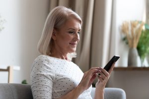 Mature woman sitting on her couch at home as she reads messages on her smartphone