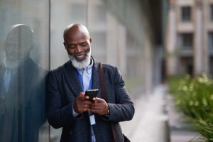 Man leaning against wall outside as he reads messages on his cell phone