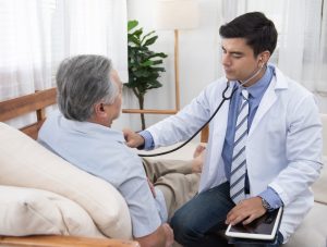 Broken heart syndrome - older man visiting with his doctor, who is listening to his patient's heart with a stethoscope