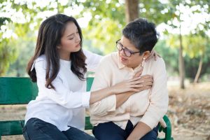 Younger woman and older woman sitting on a bench outside with the younger woman comforting as the older woman holds her hand to her chest