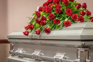 silver gray casket with casket spray of red roses lying on top