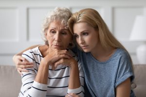 Mother and adult daughter sitting on couch, comforting each other