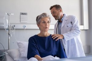 Woman sitting in a hospital bed, doctor listening to her heartbeat with a stethoscope