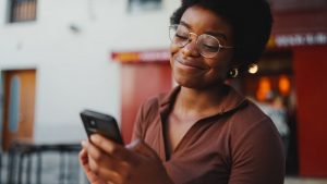 Young woman standing outside, reading smartphone messages with a gentle smile on her face