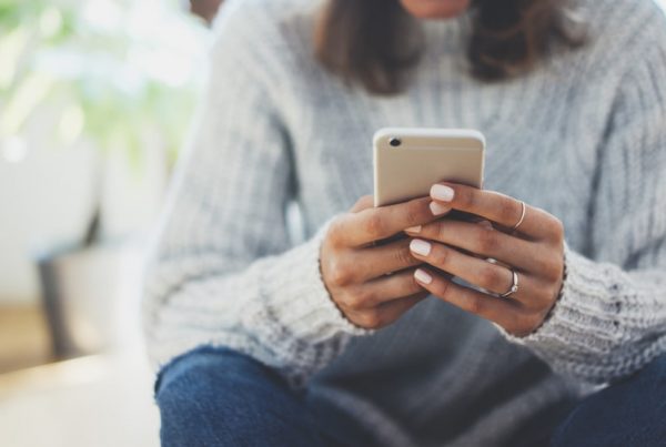 Woman with brown hair wearing a white sweater sitting down, reading messages on phone