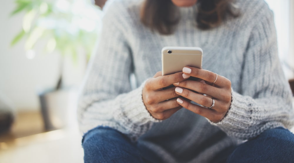 Woman with brown hair wearing a white sweater sitting down, reading messages on phone