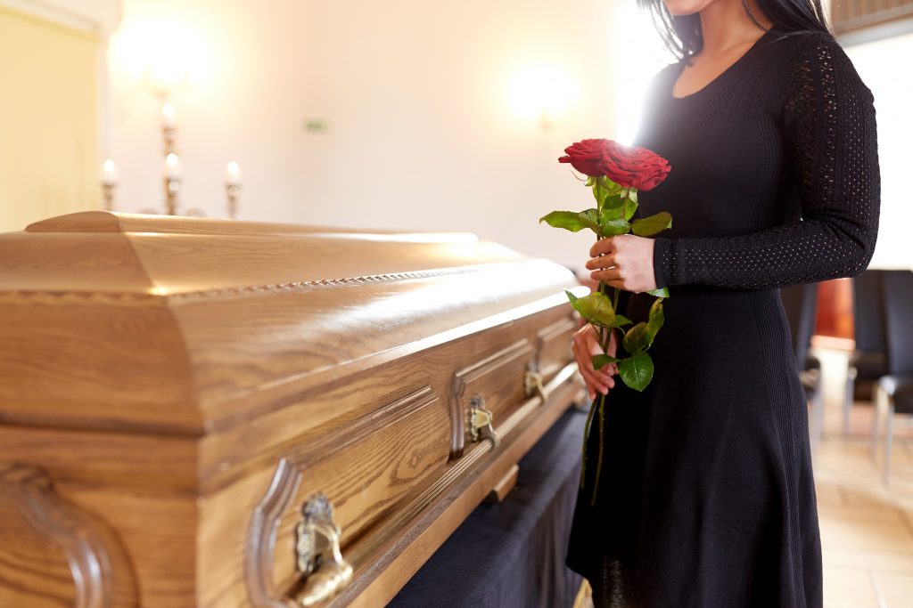 people and mourning concept - woman with red roses and coffin at funeral in church