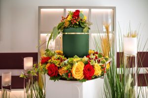 Green urn placed on pedestal surrounded by red and yellow flower garland