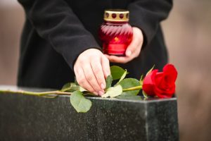 Woman in black coat leaving a red rose of remembrance on a grave marker