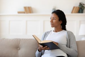 Young woman sitting down as she holds an open book and looks to the left