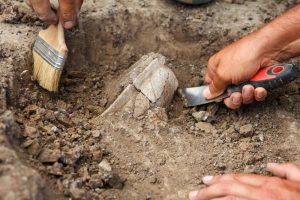 Shows archeologists using brushes and tools to excavate a historical site