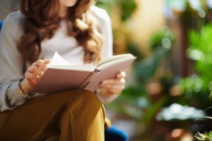 Woman with brown hair sitting outside as she reads a book