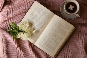 Open book laying on a pink blanket with white flowers resting on its pages