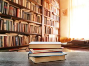 Four books in a stack on a table in front of several bookcases