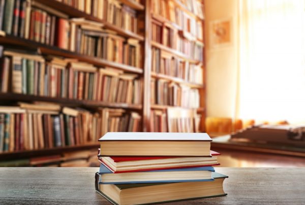 Four books in a stack on a table in front of several bookcases