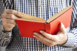 Older man holding an open red book, with his fingers prepared to turn the page