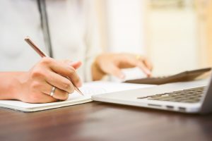 Person in white shirt, sitting at desk, with pen in hand as they review paperwork