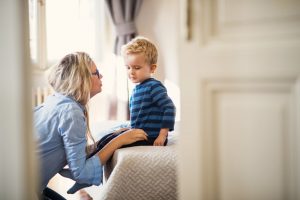Blonde mother kneeling in front of young son, talking softly to him