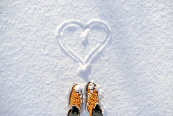 Person standing in front of a heart drawn into the snow during the holiday season