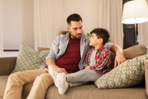 Father and son sitting on tan couch at home, talking together