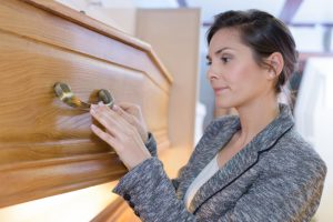 Middle-aged woman in gray suit jacket touching and inspecting a casket