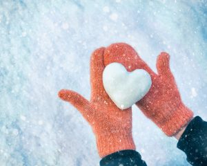 Person wearing orange gloves and holding a heart-shaped snowball during holiday season