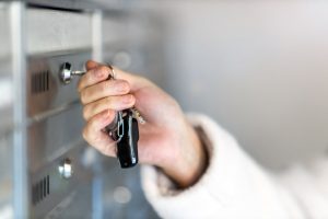 Person in white jacket using a key to open a mailbox