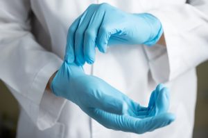 Person putting on blue disposable gloves, wearing white lab coat