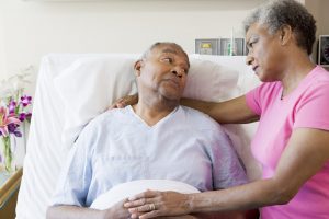 Man lying in hospital bed, talking to caring wife