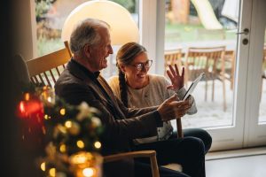 Mature couple sitting near Christmas tree as they talk with family through video chat