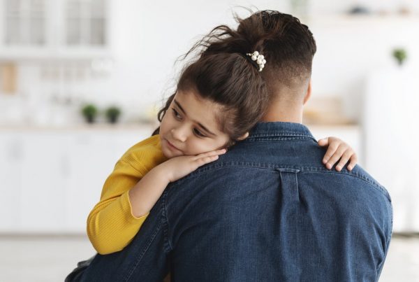 Father in denim shirt comforting his young daughter, who is sad