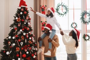 Family of three - dad, mom, and pre-teen daughter - putting up Christmas tree together at holiday