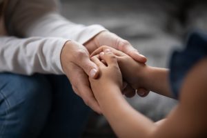 Focus on the hands of two people, a female adult gently holding the hands of a child who needs comfort